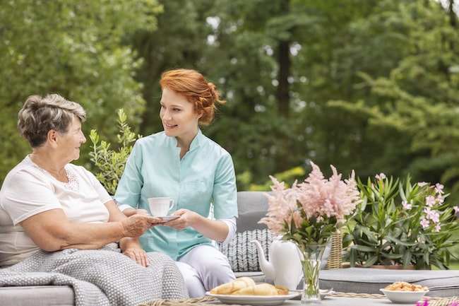 happy-nurse-giving-tea-to-elderly-woman-while-eating